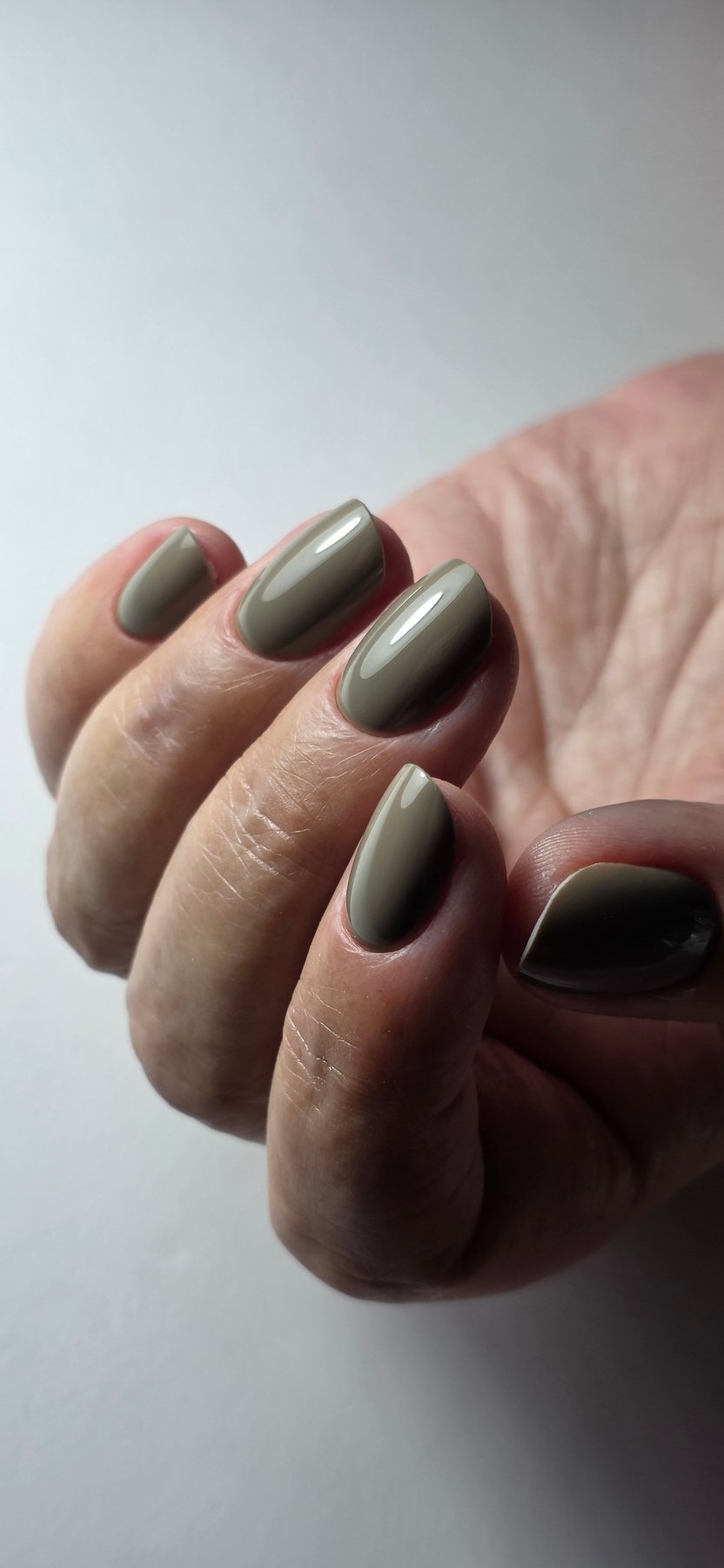 Pose du Gel Polish Mystic taupe kaki sur ongles ovales courts, fond blanc épuré