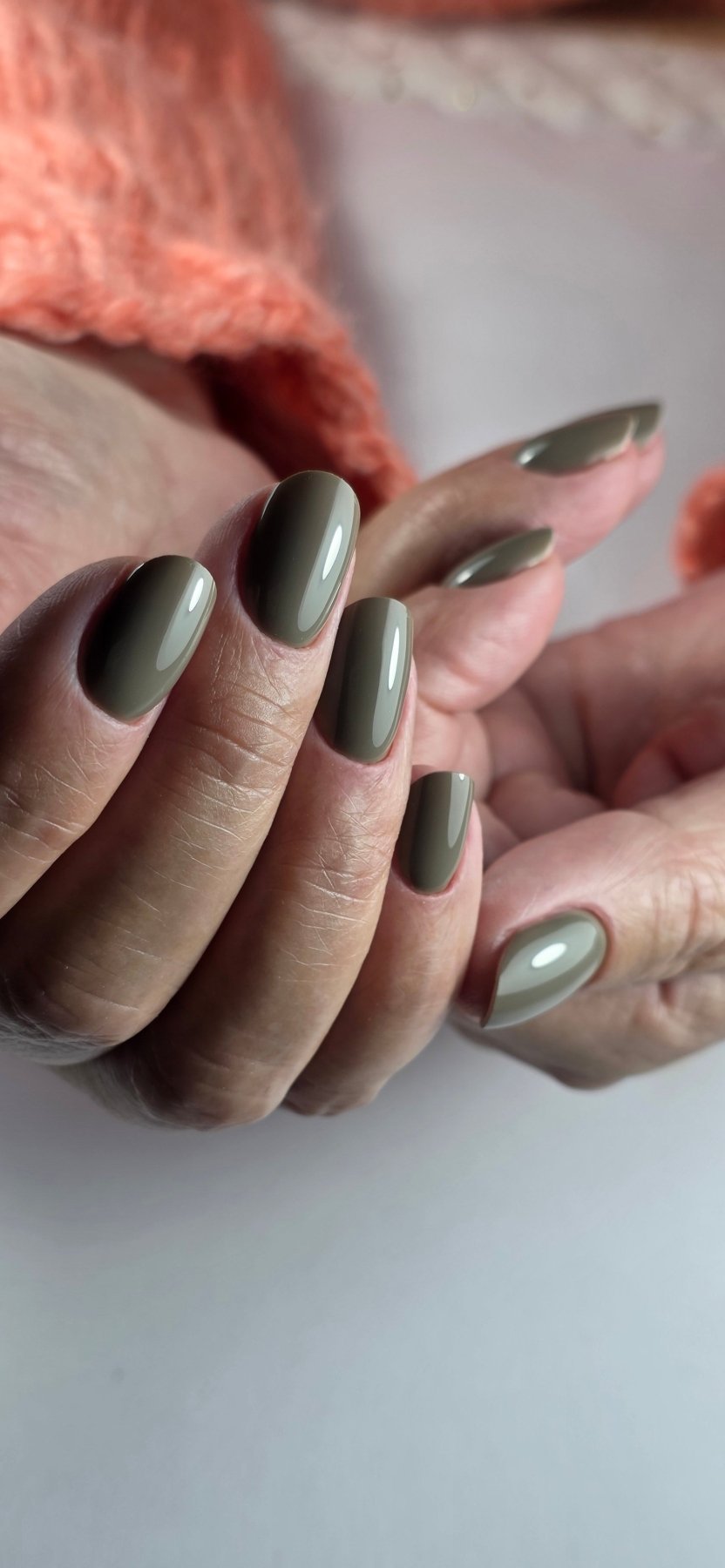 Gel Polish Mystic taupe kaki sur ongles en amande, mains posées près d'un pull corail