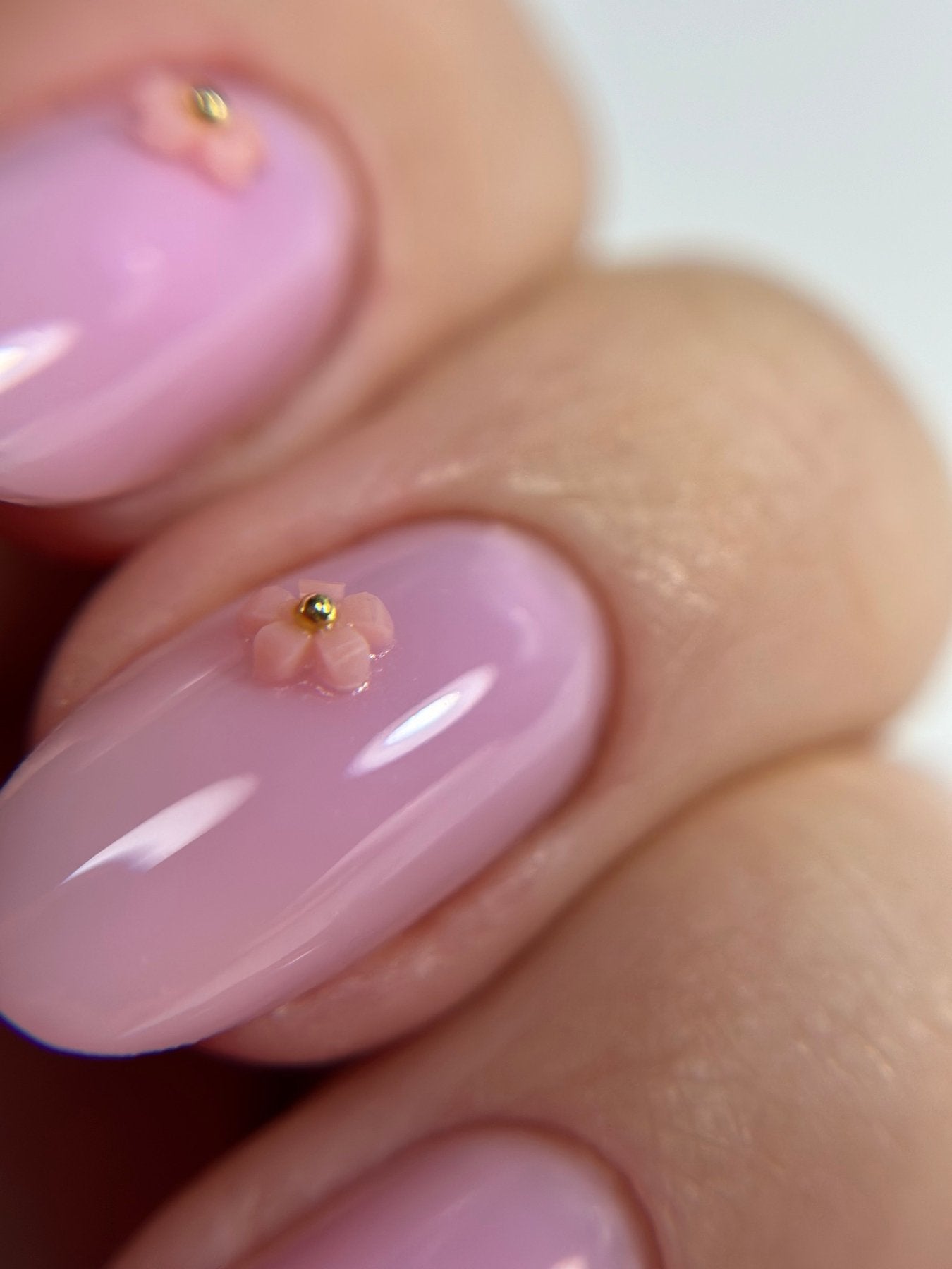 Gros plan de la Cloud base Romy rose lilas sur ongles ovales, fleurs 3D et perle dorée
