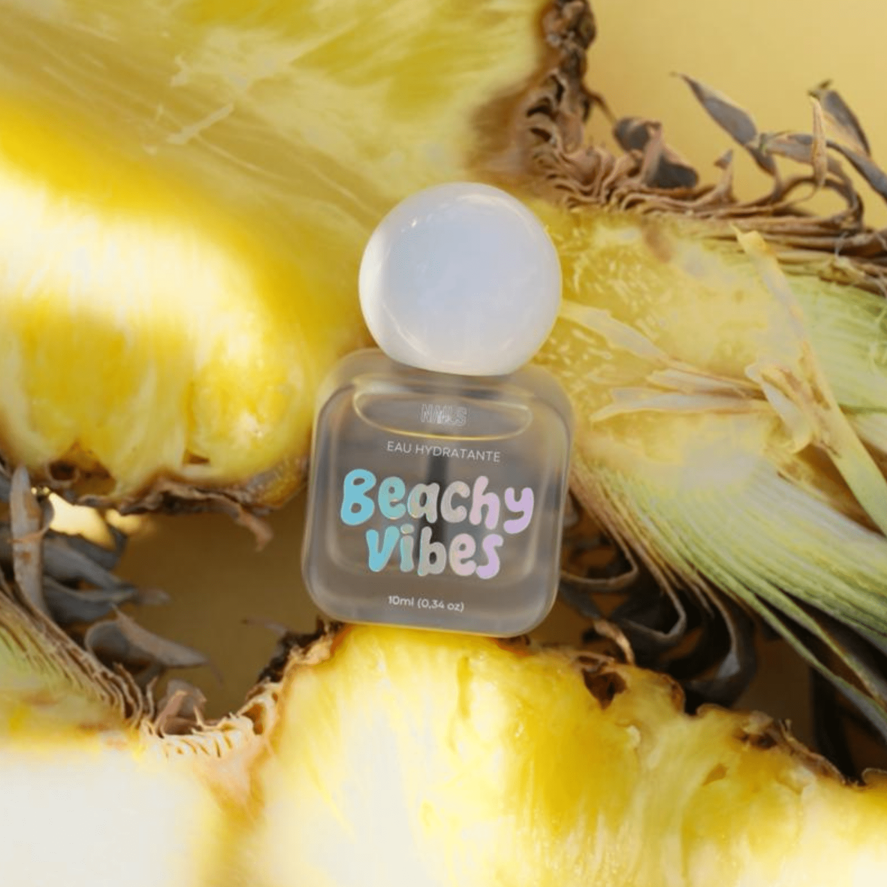 Eau hydratante cuticules Beachy Vibes posée sur un ananas ouvert, fond jaune ensoleillé