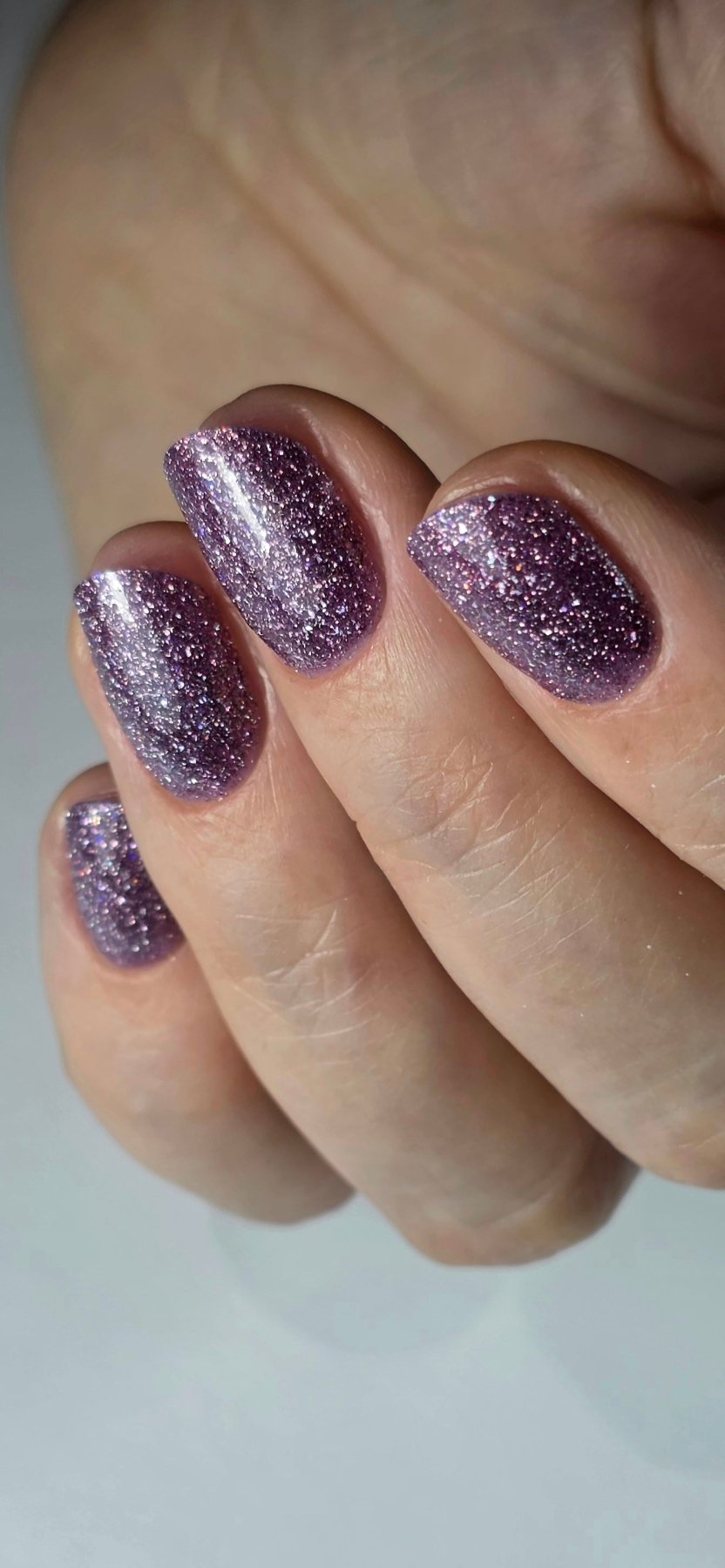 Pose du Gel Polish Kitty violet parme pailleté sur ongles carrés courts, main fermée