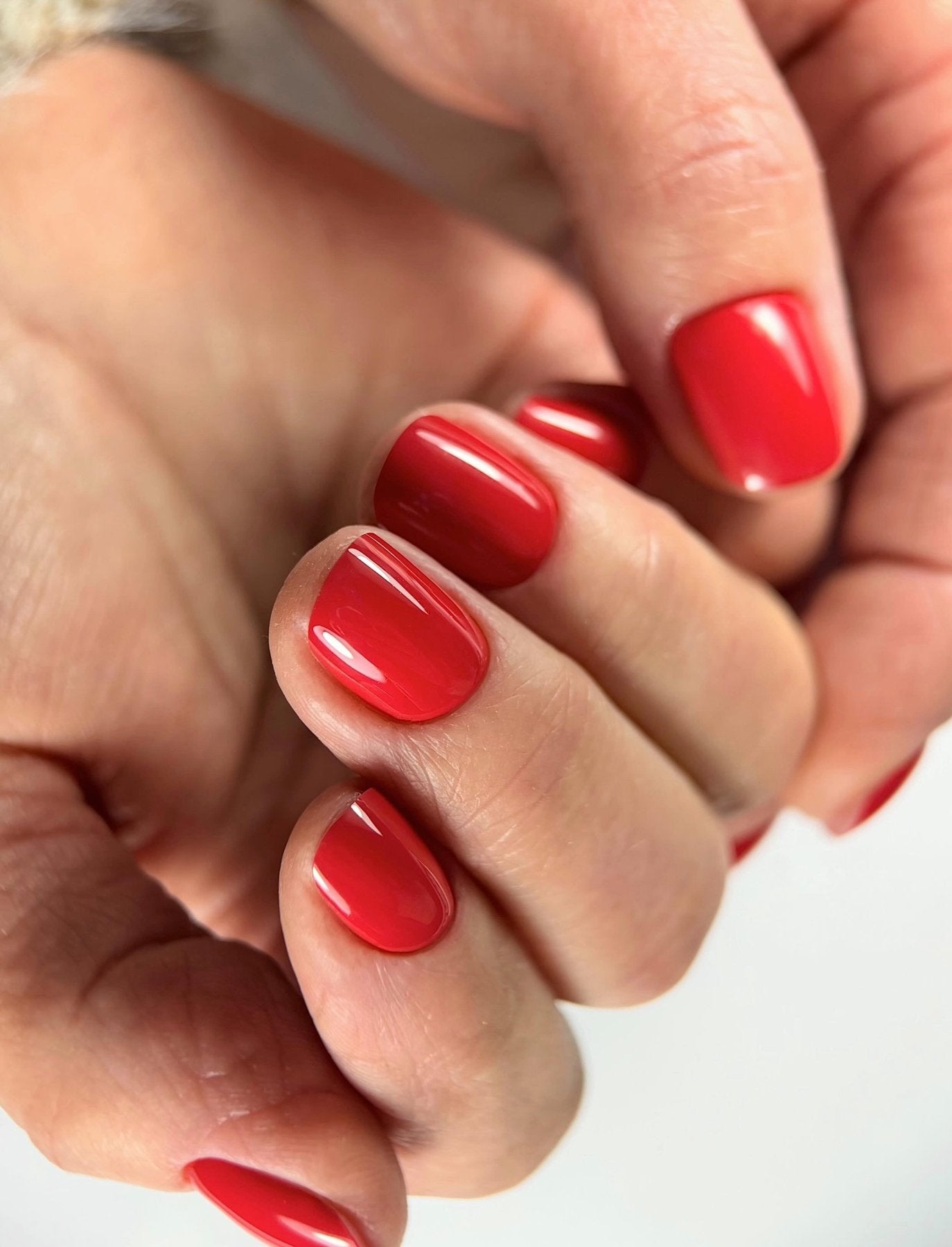 Gel Polish Candy Cane rouge cerise sur ongles courts carrés, gros plan sur une main fermée