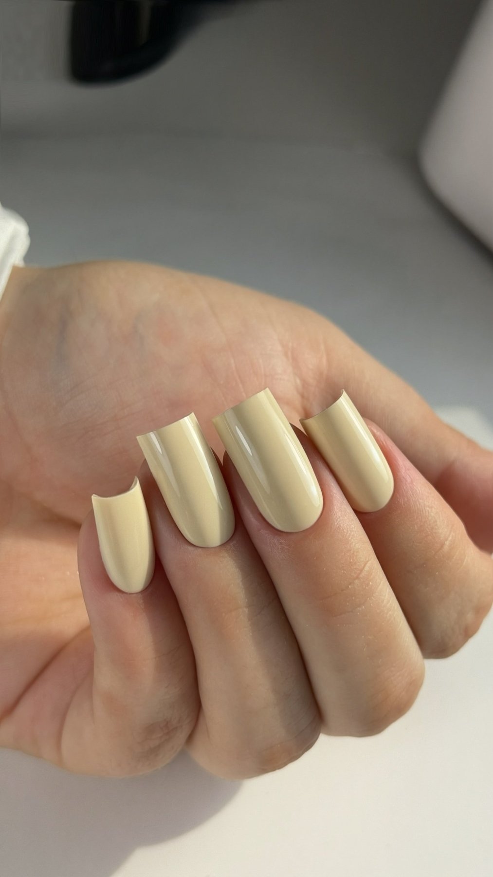 Gel Polish Promise jaune vanille sur ongles carrés, main fermée sur fond clair