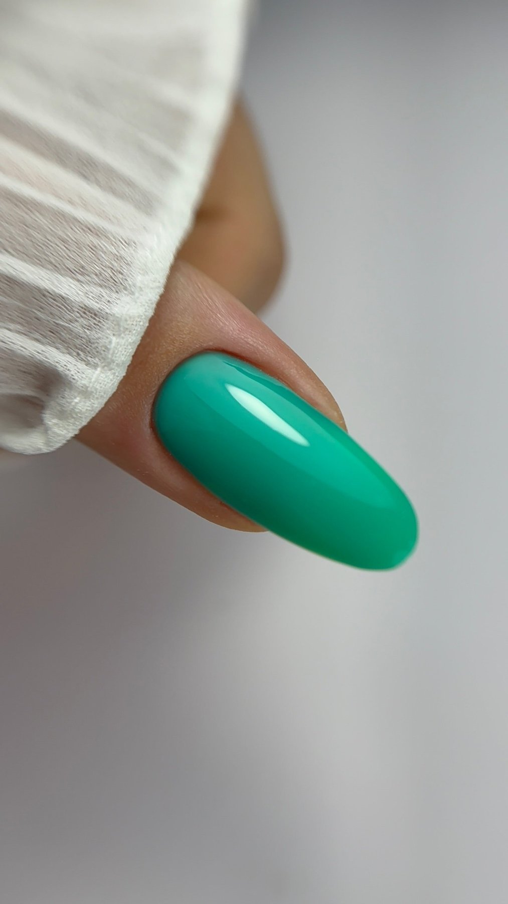 Gros plan d'un ongle amande recouvert de Cloud base Noa vert turquoise, fond gris