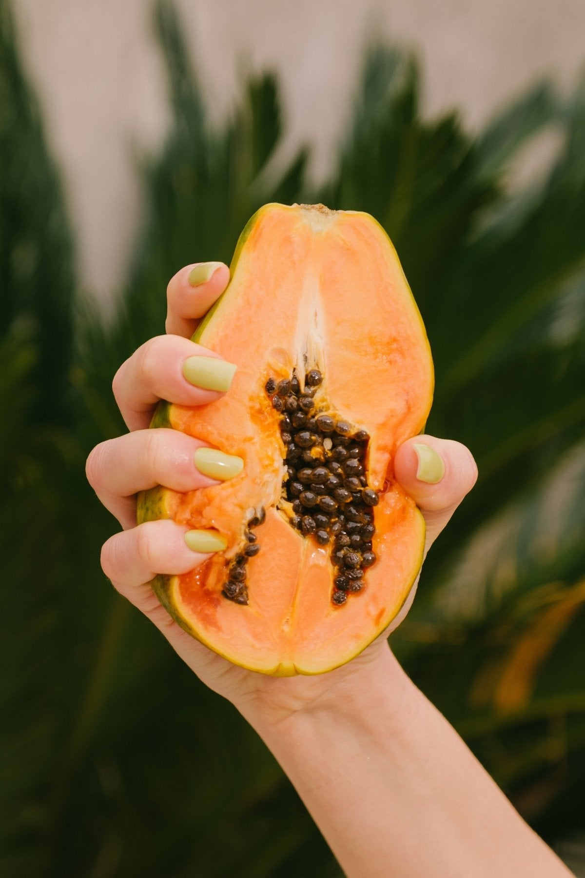 Ongles jaune citron au Gel Polish Limonada tenant une papaye coupée, décor tropical