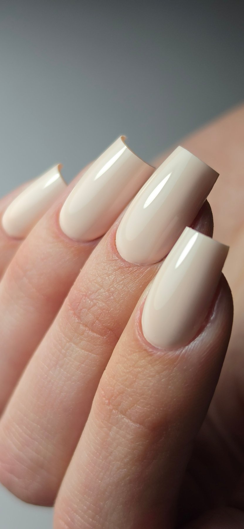 Macro du Gel Polish Bride rose ivoire sur ongles carrés longs, fond gris uni