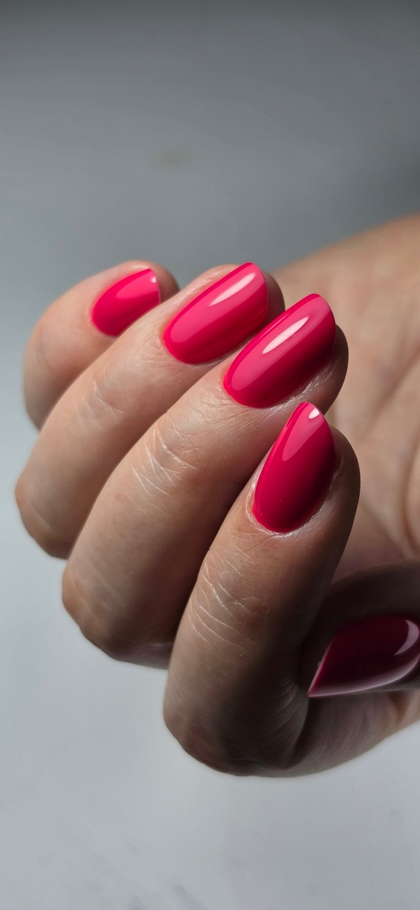 Pose du Gel Polish Samba rose magenta sur ongles en amande courts, fond gris clair