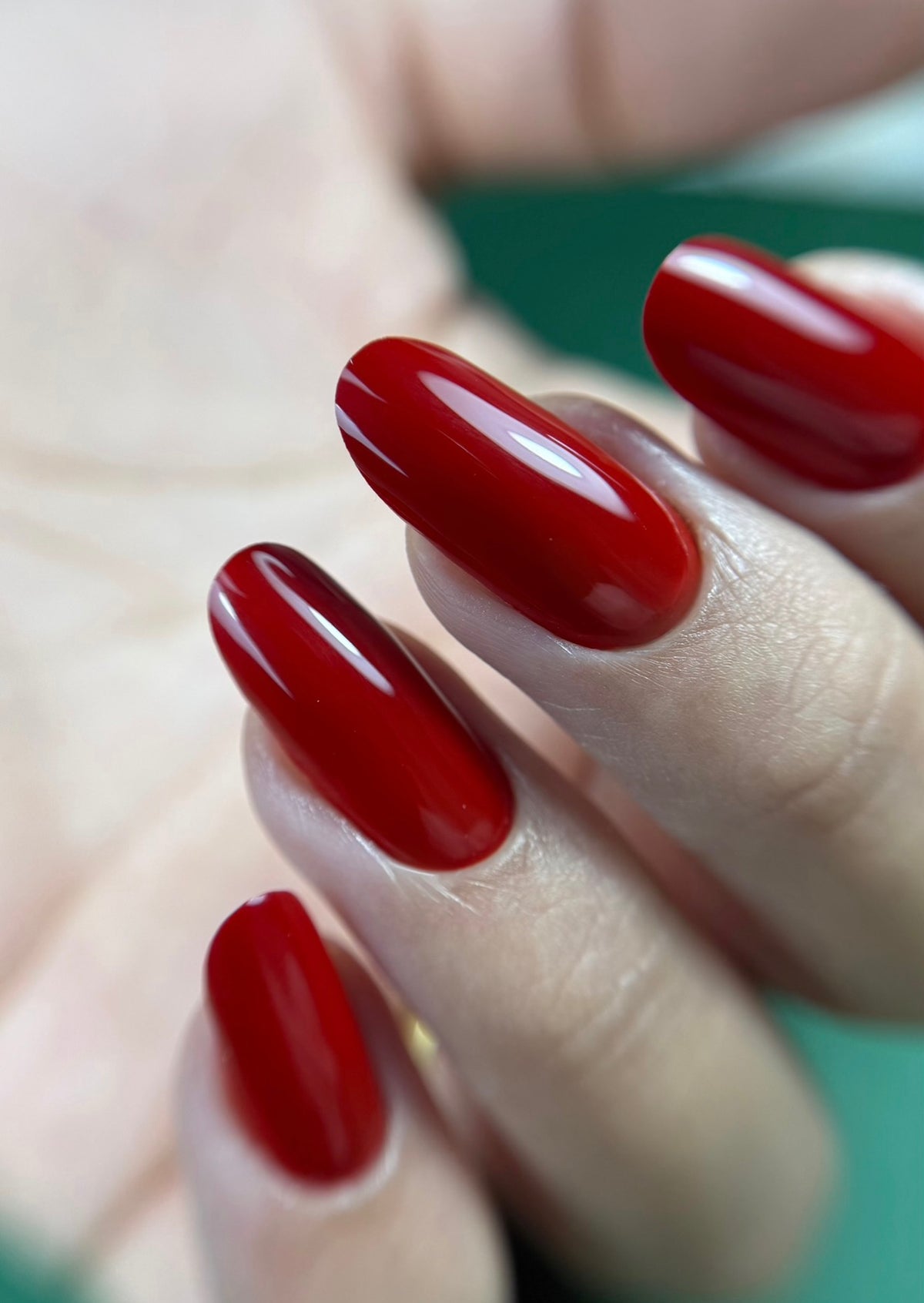 Pose du Gel Polish Wine rouge brique sur ongles longs ovales, fond vert émeraude