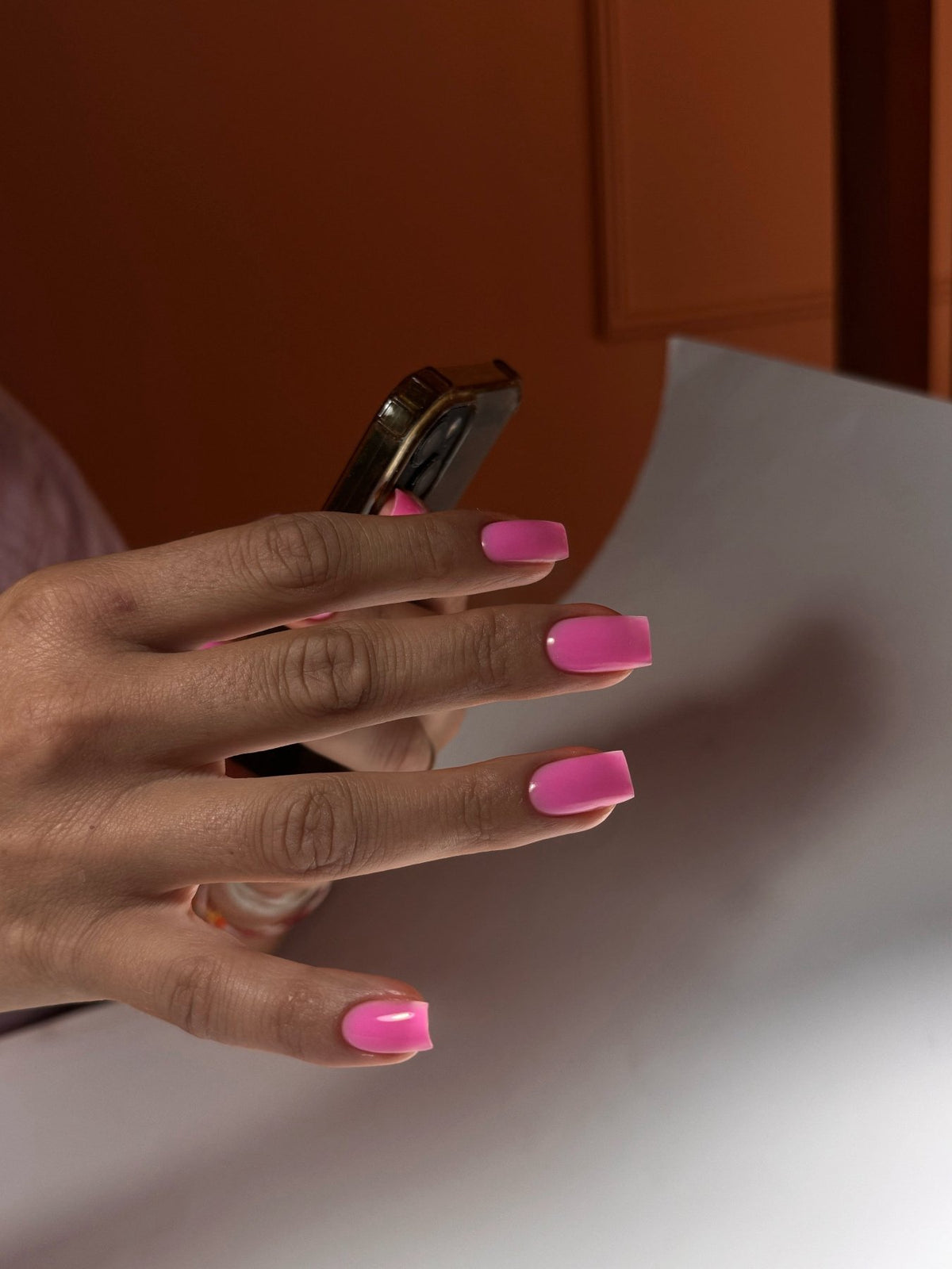 Ongles carrés au gel Easy gel Rio, rose fuchsia vif, main tenant un téléphone