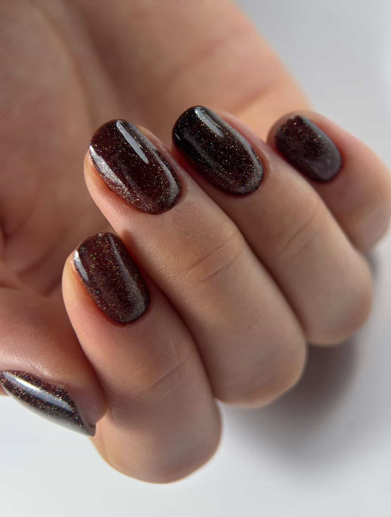 Gel Polish Brownie chocolat pailleté sur ongles courts arrondis, gros plan sur fond blanc