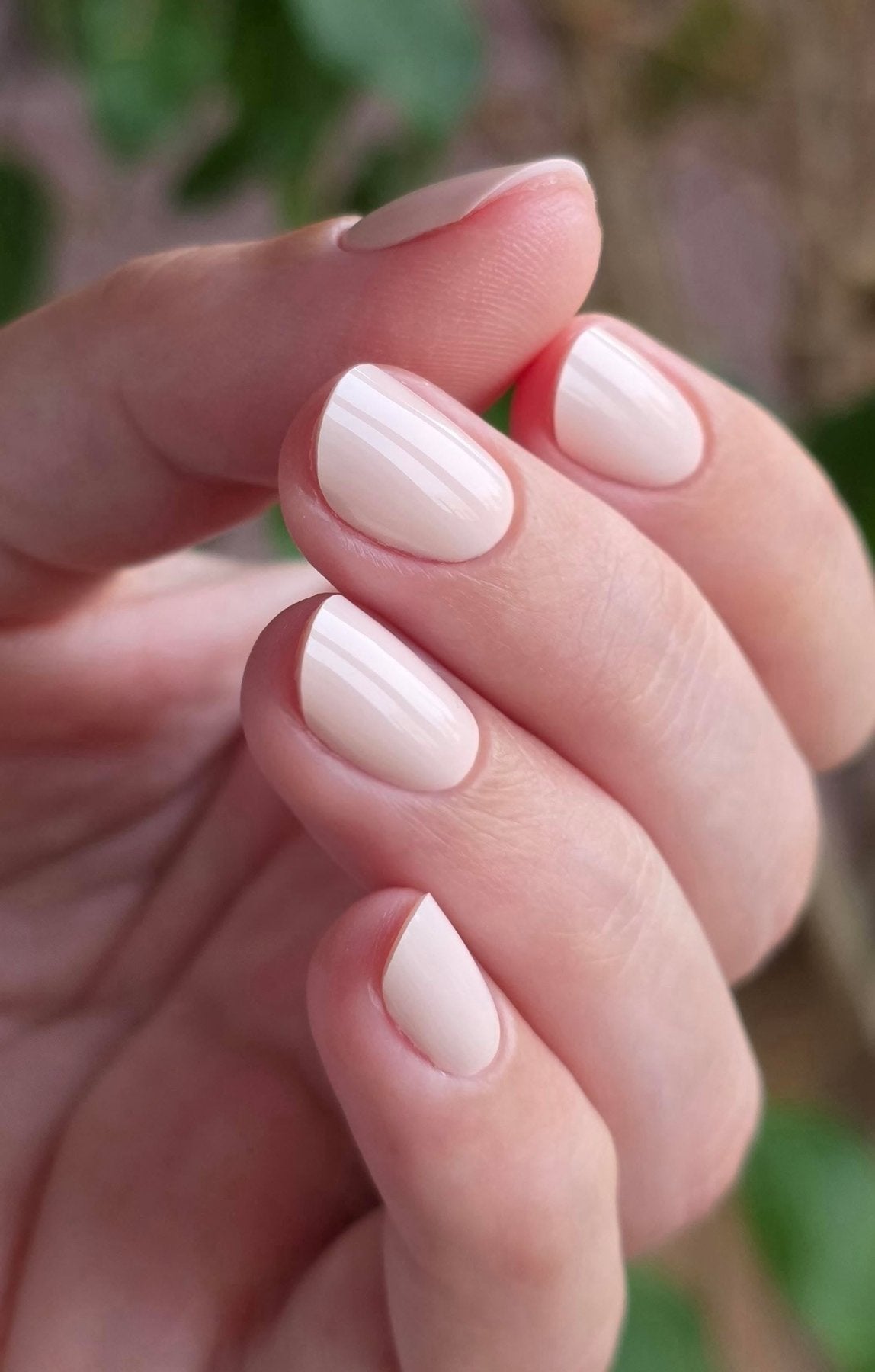 Pose du Gel Polish Bride rose ivoire laiteux sur ongles ovales courts, fond de feuillage