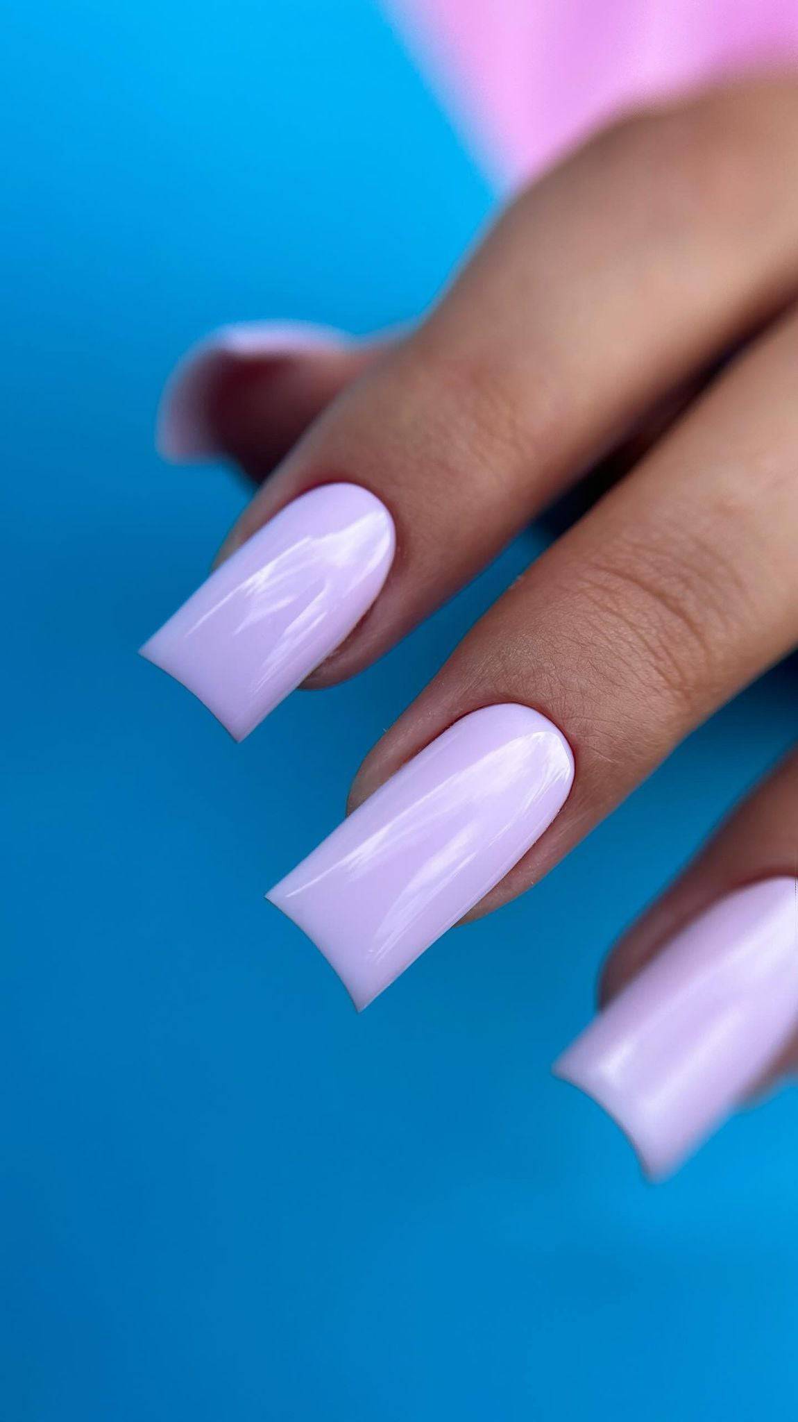 Pose du Gel Polish Camille rose lilas sur ongles carrés longs, fond bleu vif