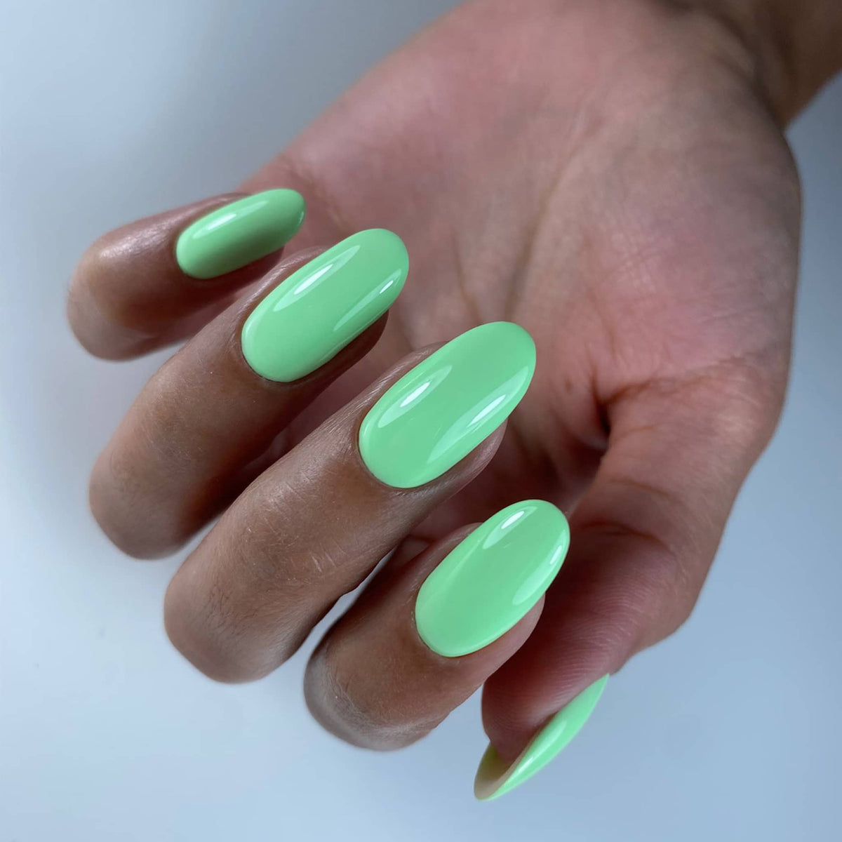 Pose du Gel Polish Jacuzzi vert menthe sur ongles longs en amande, fond bleu clair