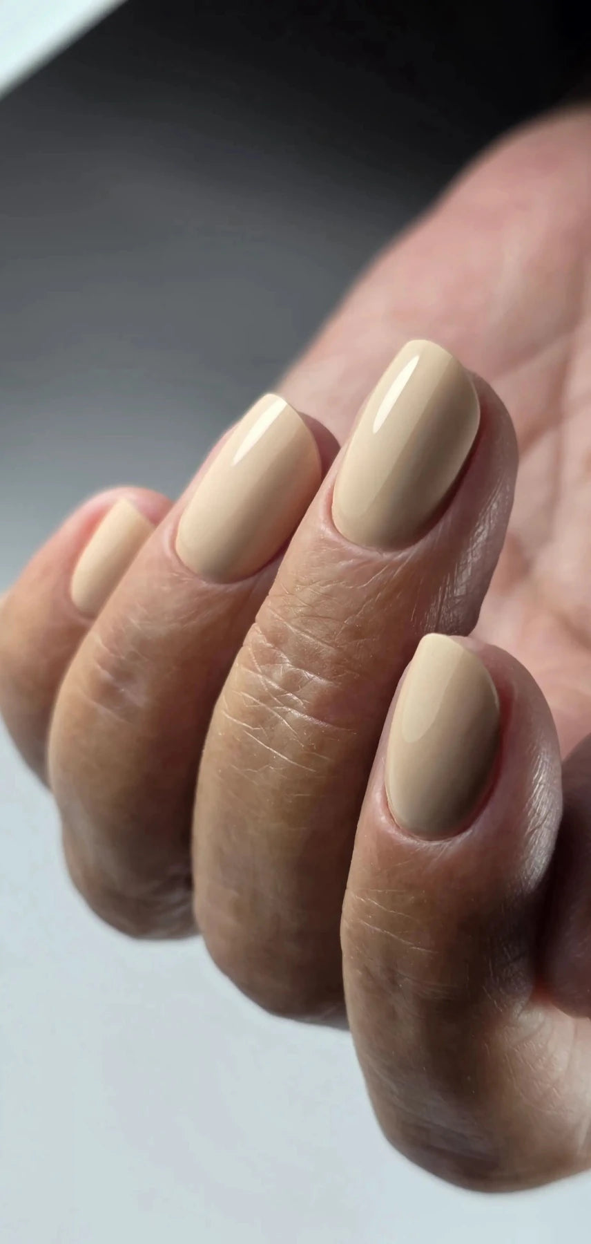 Pose du Gel Polish Ceremony beige sable sur ongles ovales courts, fond gris clair