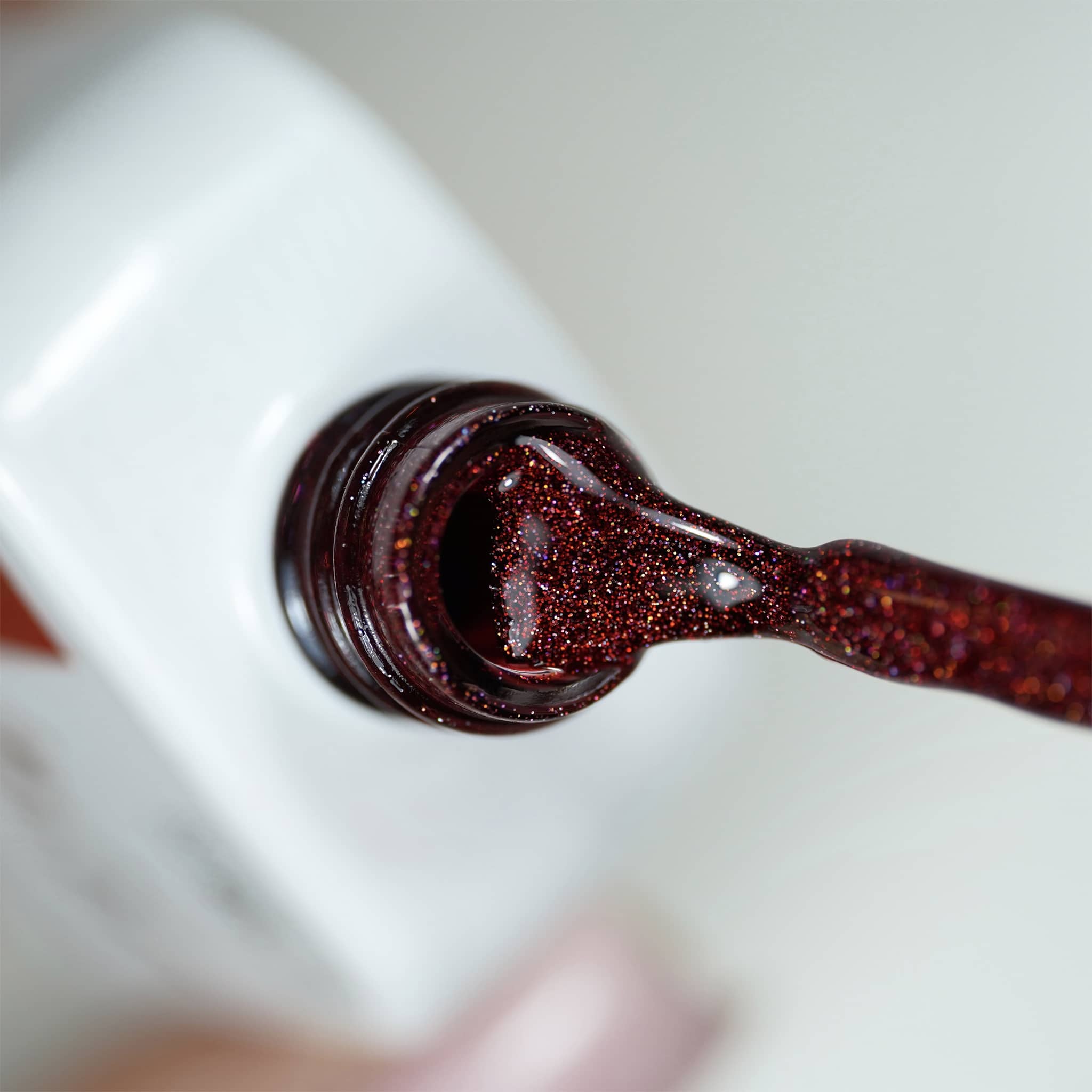 Pinceau et goulot du Gel Polish Amor, texture bordeaux crémeuse aux paillettes cuivrées