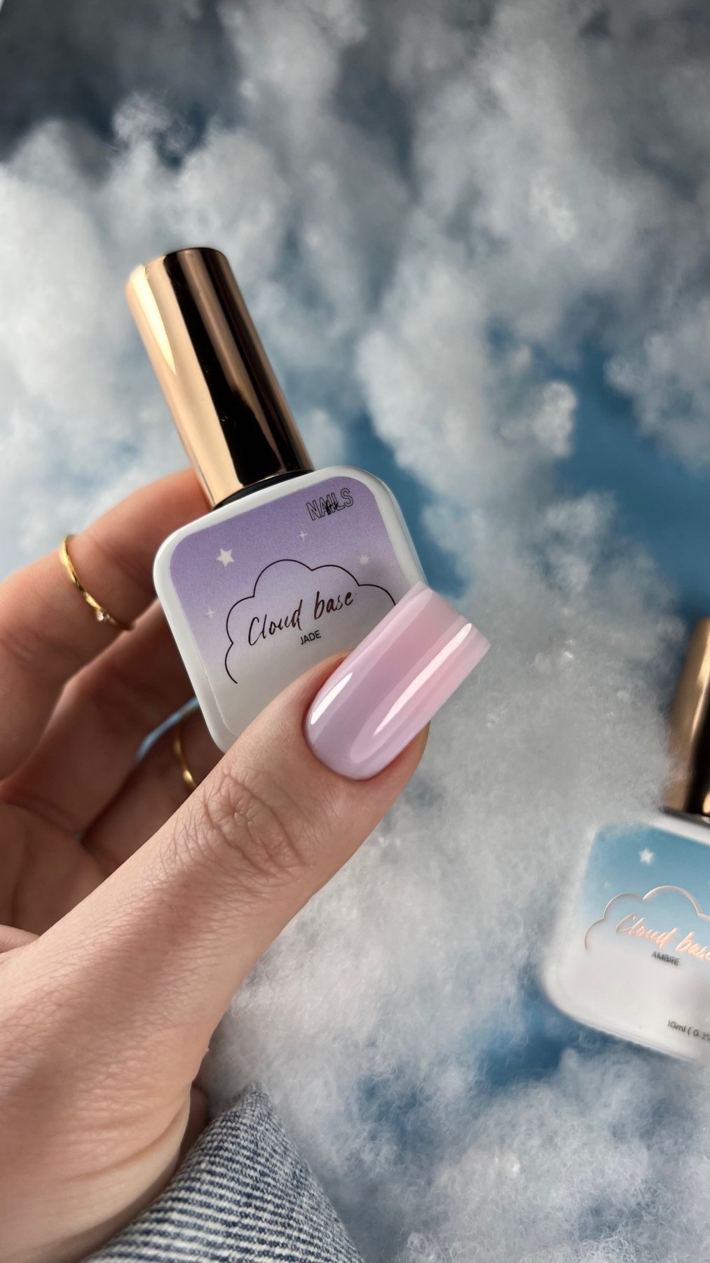 Flacon de la Cloud base Jade tenu en main, ongle carré lilas pâle et décor nuages