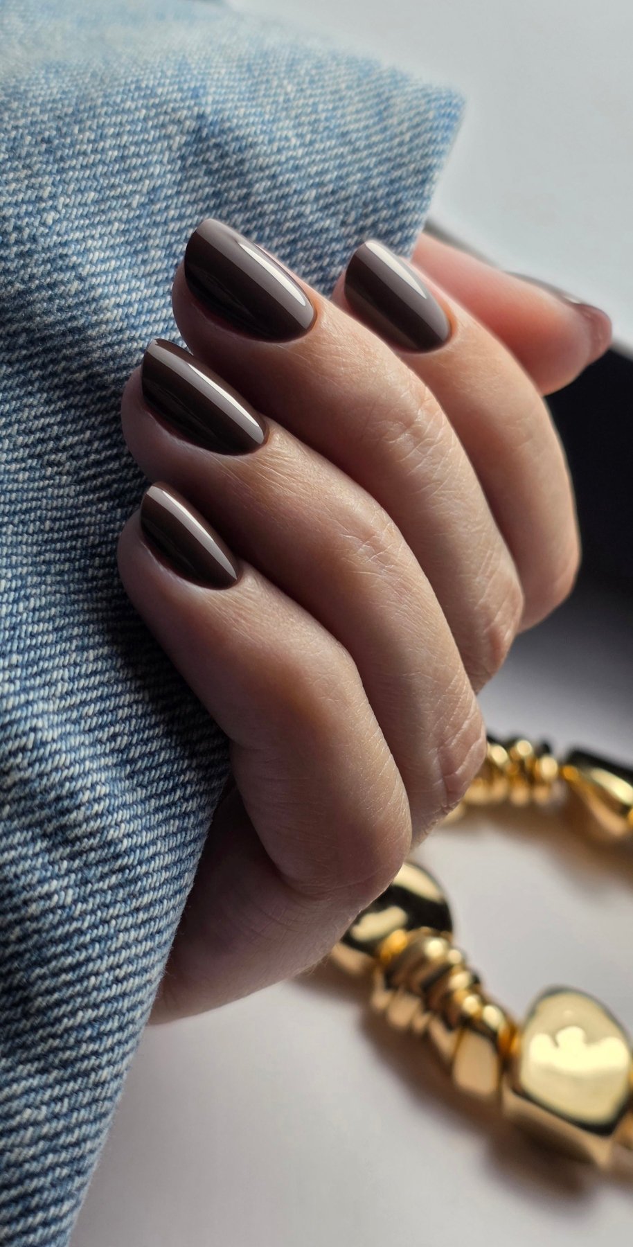 Gel Polish Mocha marron moka sur ongles ovales courts, bracelet doré et manche en jean