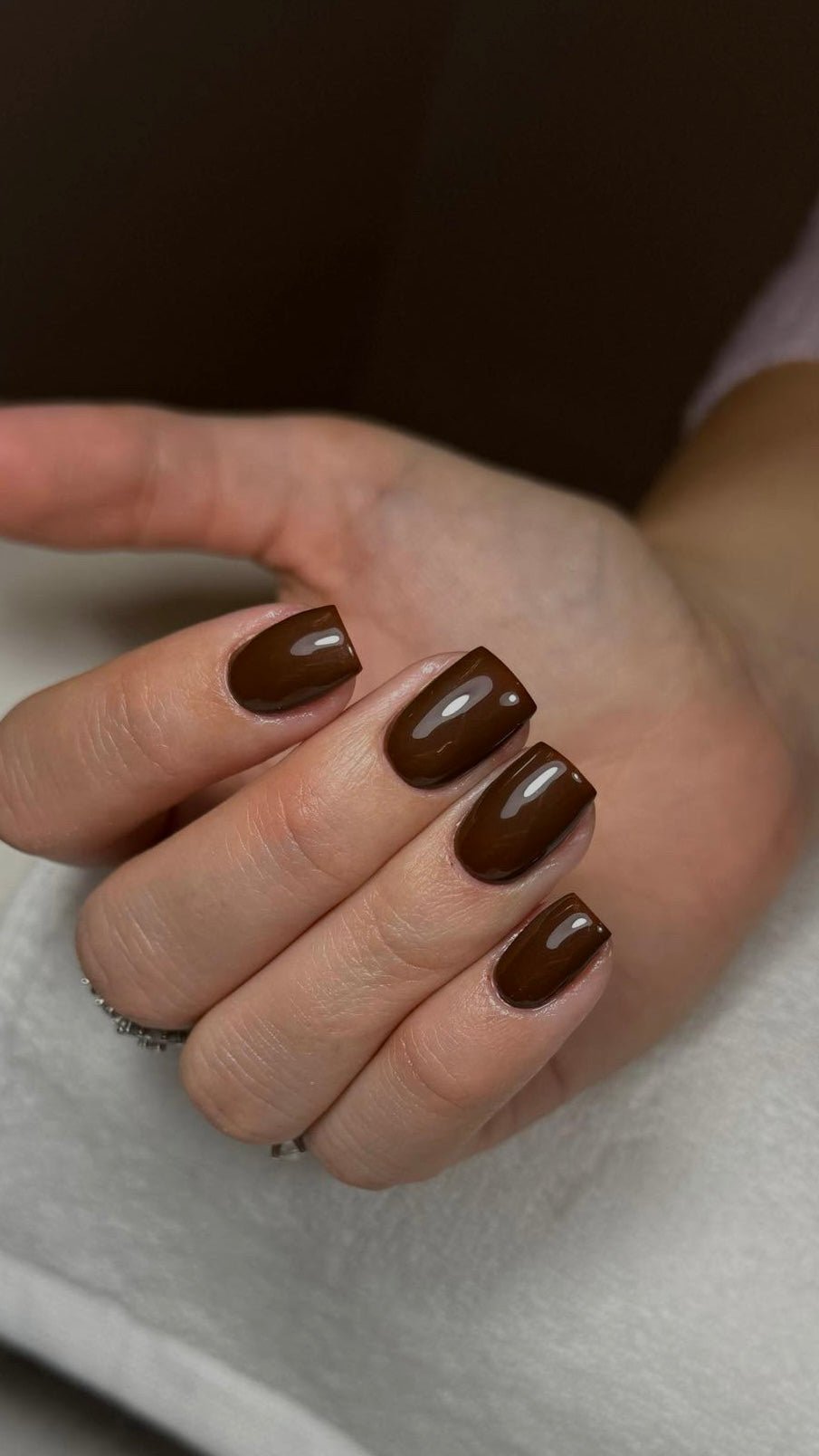 Pose du Gel Polish Espresso chocolat sur ongles carrés, main posée sur une serviette blanche