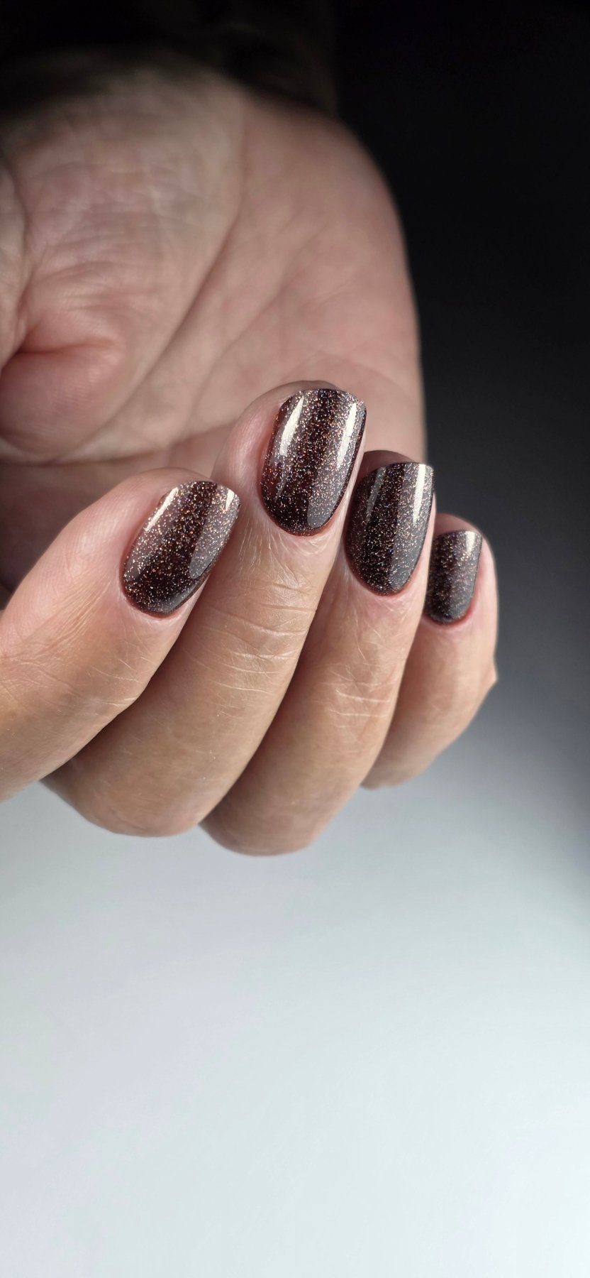 Pose du Gel Polish Brownie chocolat pailleté sur ongles ovales, fond dégradé sombre