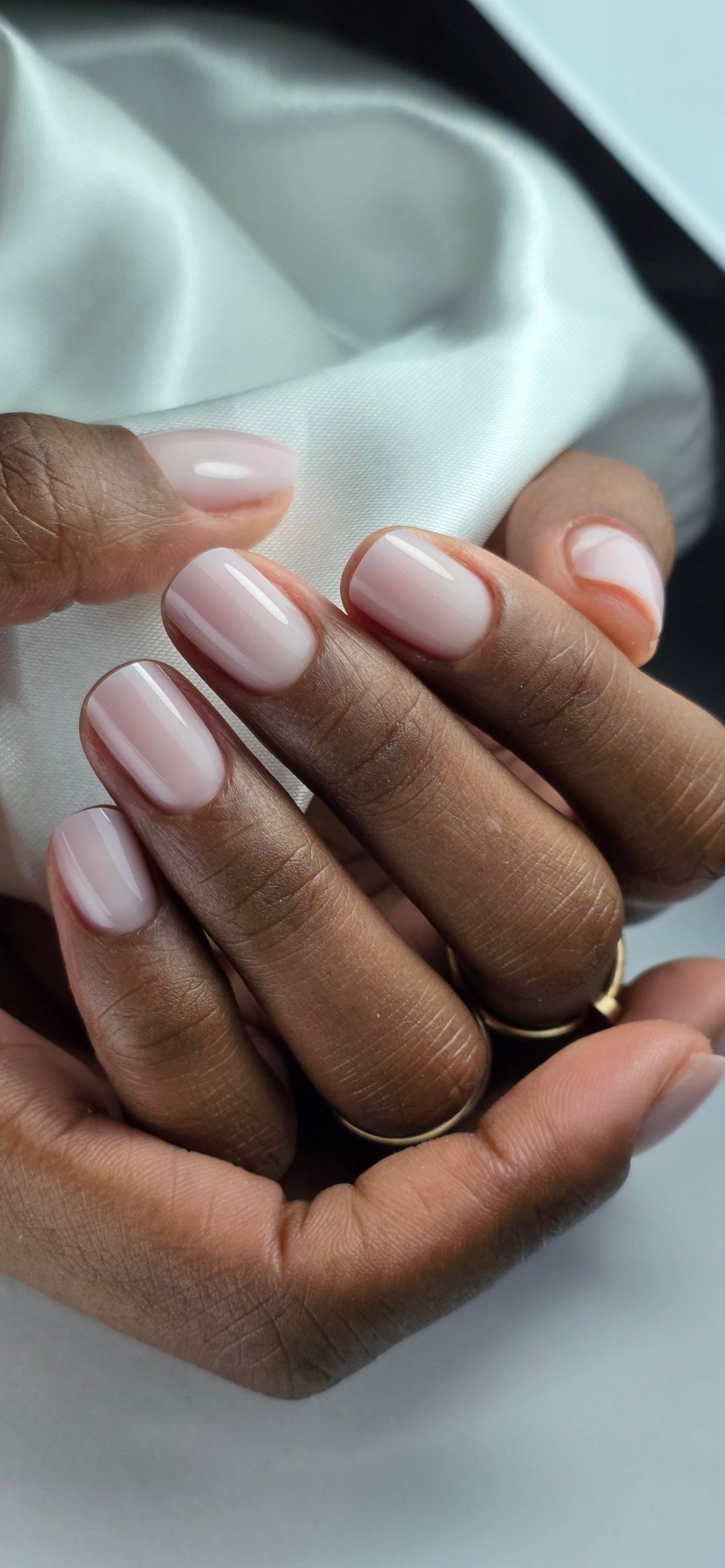 Ongles courts au gel Solid fiber Vanilla sur peau foncée, rose laiteux devant un satin blanc