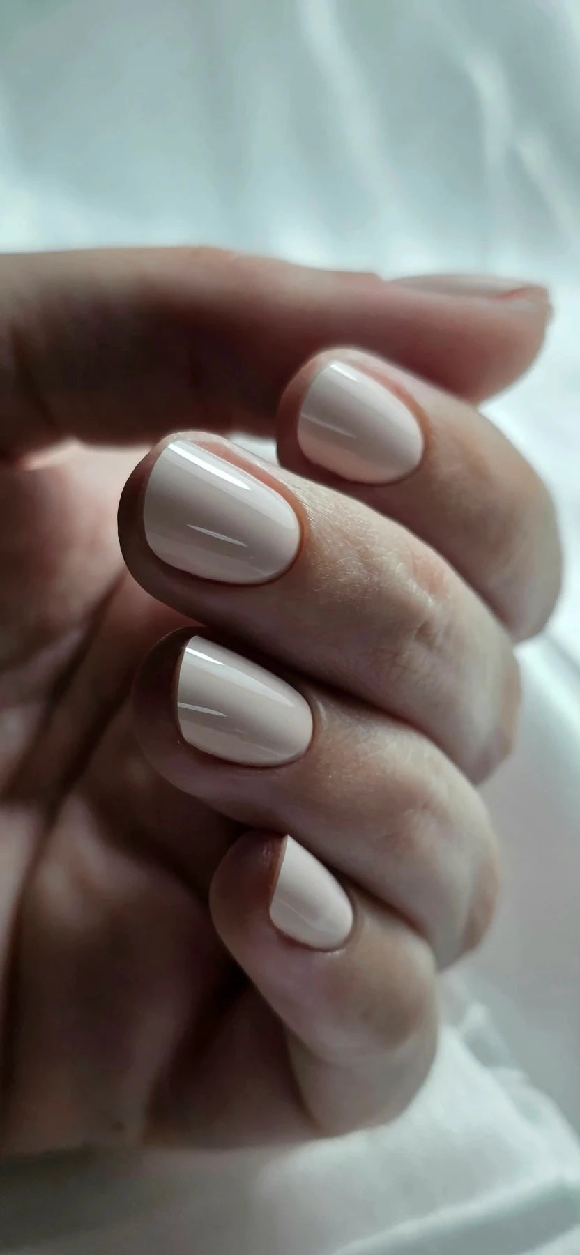 Pose du Gel Polish Bride rose ivoire sur ongles ovales courts devant un drapé blanc
