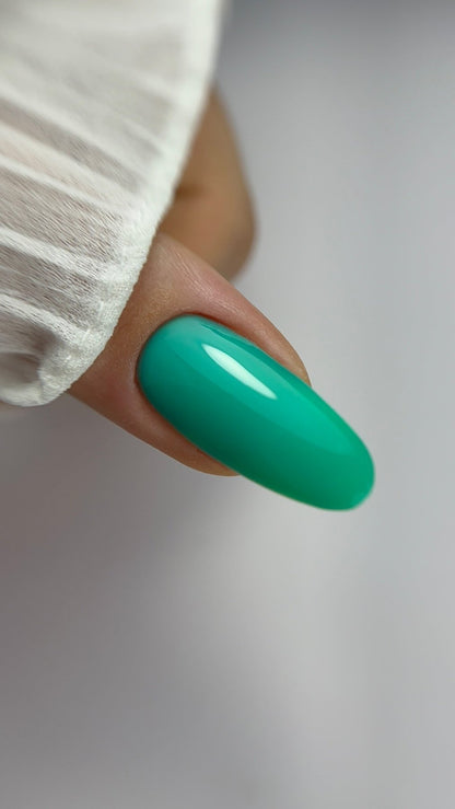 Gros plan d'un ongle amande recouvert de Cloud base Noa vert turquoise, fond gris