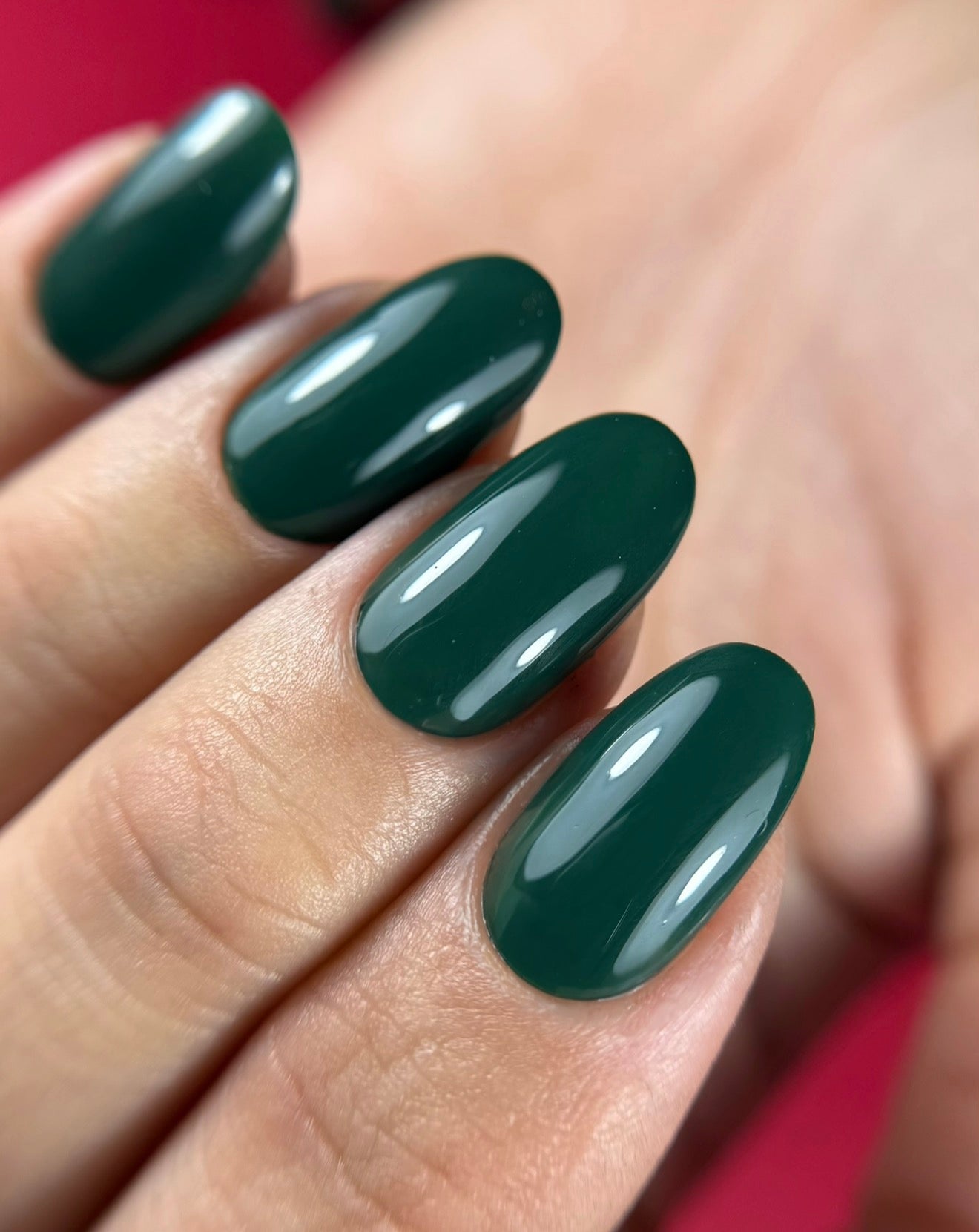 Pose du Gel Polish Venom vert sapin foncé sur ongles ovales, fond rose framboise