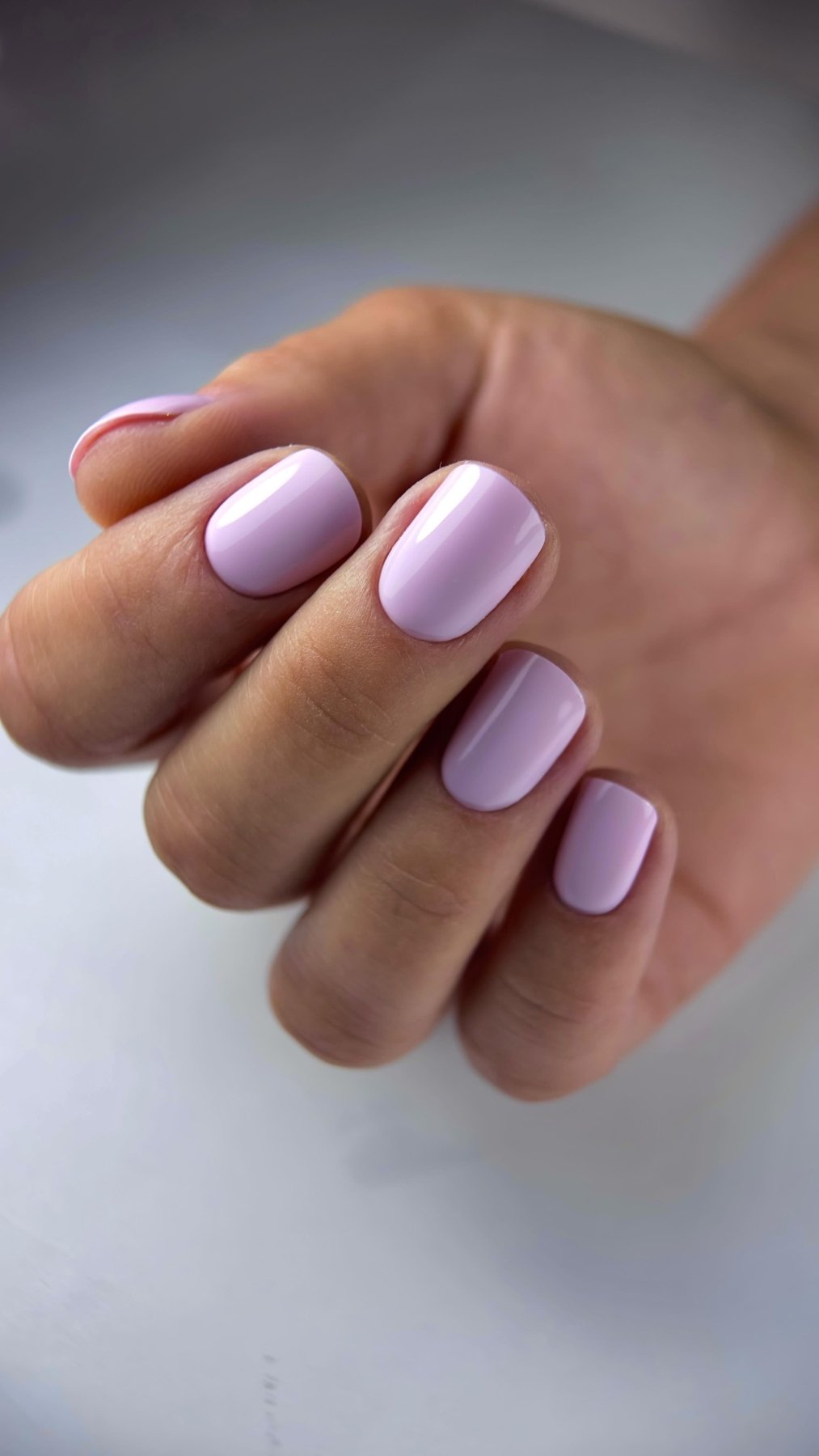Pose du Gel Polish Camille rose lilas sur ongles carrés courts, main fermée sur fond blanc