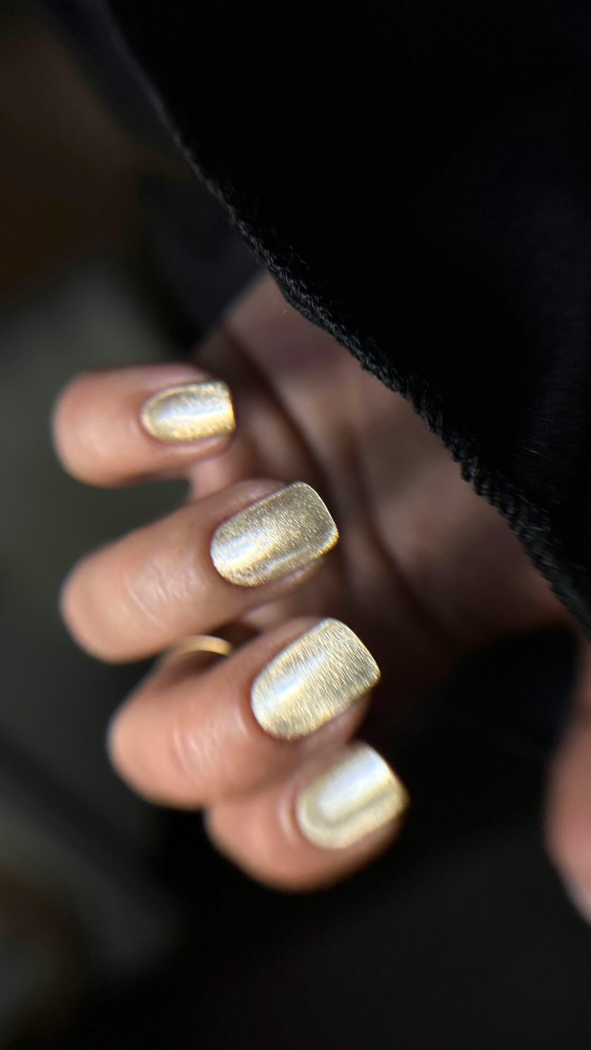Gros plan de l'effet cat eye doré du Gel Polish Mahalo sur ongles carrés, ambiance sombre