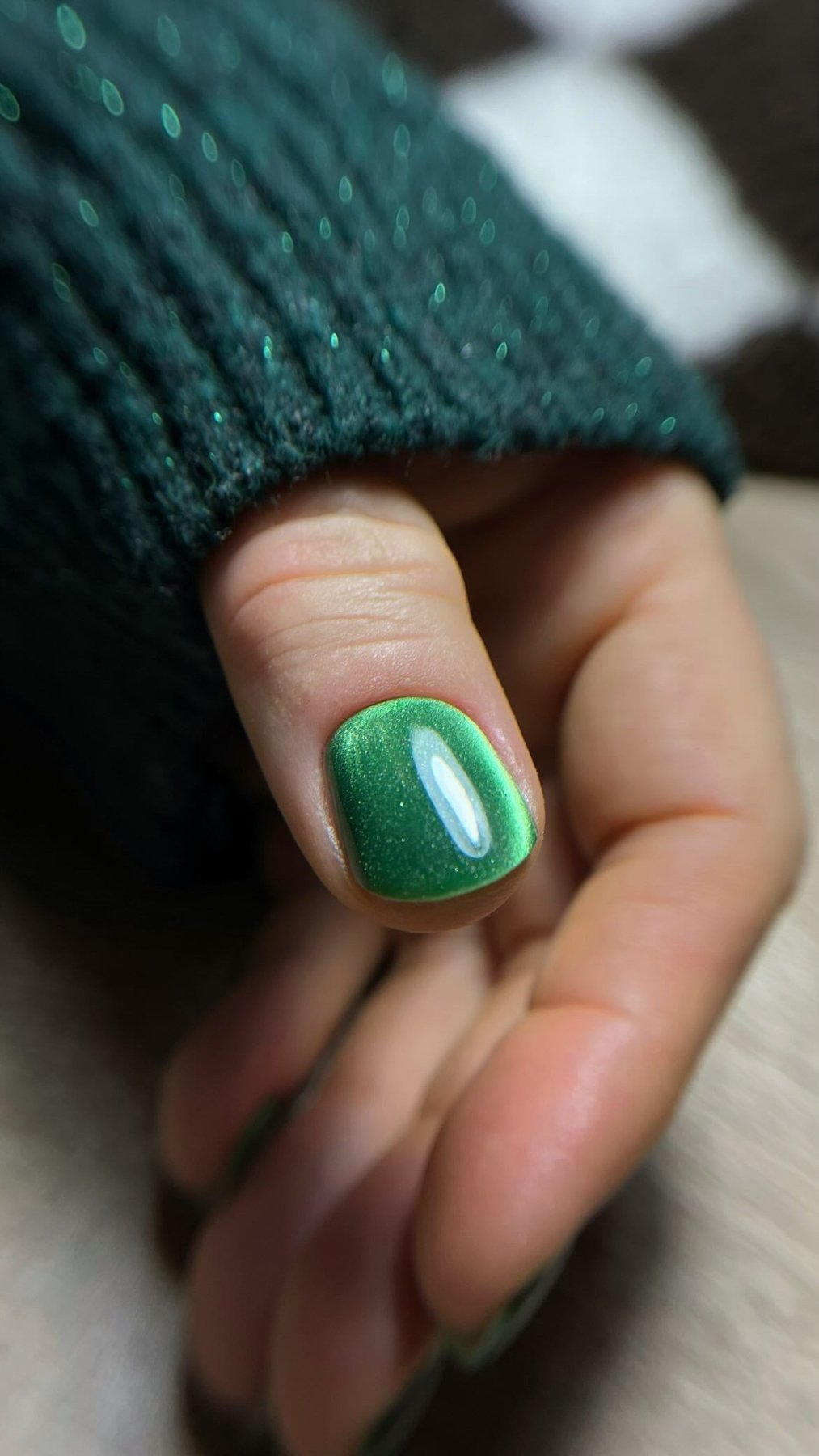 Pose du Gel Polish Midnight Green vert nacré sur ongle court, manche d'un pull vert pailleté
