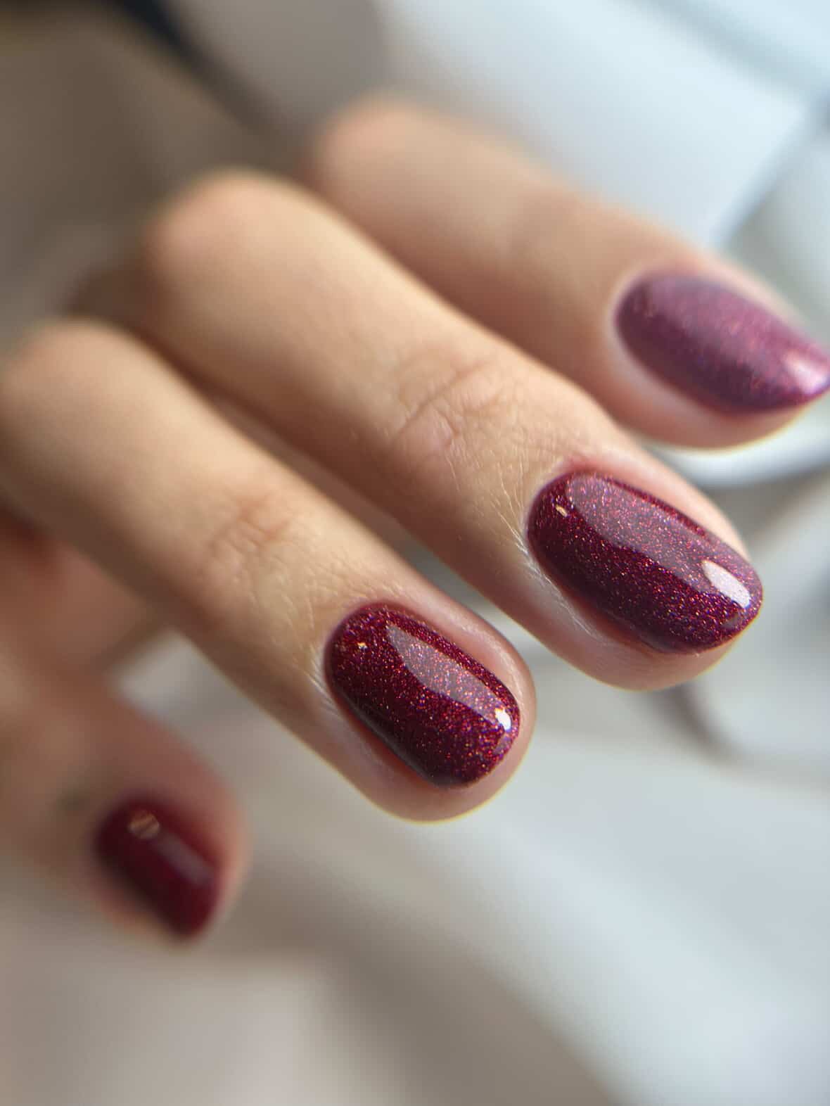 Pose du Gel Polish Love bordeaux pailleté sur ongles courts ovales, reflets holographiques