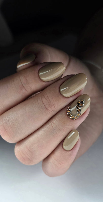 Pose du Gel Polish Cream beige nude sur ongles ovales, un ongle orné de strass ambrés