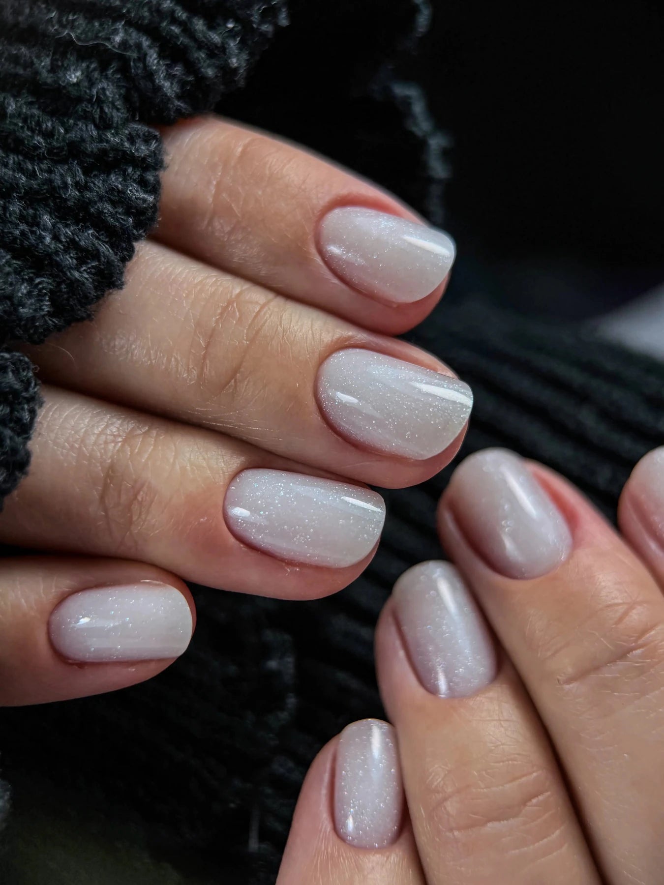 Deux mains aux ongles courts au gel Solid fiber milky shine, blanc nacré, sur pull noir