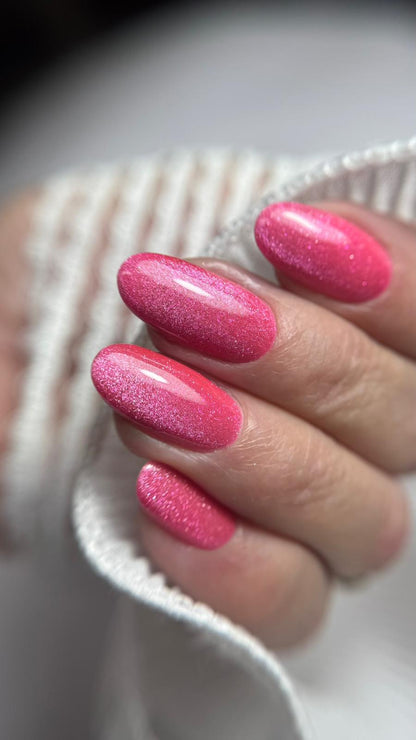 Pose du Gel Polish Leï fuchsia pailleté sur ongles en amande, fond de pull blanc