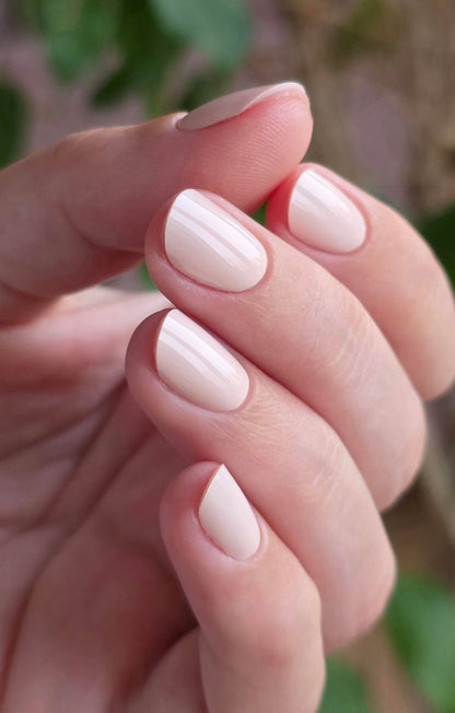 Pose du Gel Polish Bride rose ivoire laiteux sur ongles ovales courts, fond de feuillage