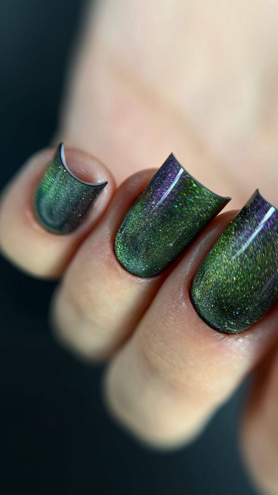Gros plan de l'effet cat eye du Gel Polish Lueur, reflets vert et violet sur ongles carrés